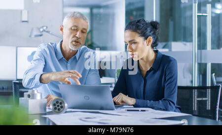 Experienced Male and Female Industrial Engineers have Discussion, Making Adjustment and Perfecting Parts, Type Corrections on a Laptop Stock Photo