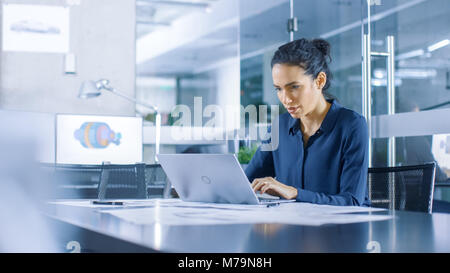 Beautiful Female Data Analyst sitting at the Table Works on a Laptop. Stylish Woman in the Modern Office Environment. Stock Photo