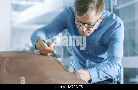 Experience Automotive Designer with a Rake Sculpts Prototype Car Model from Plasticine Clay. He Works in a Modern Studio in a Major Automotive Company Stock Photo