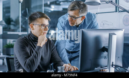 Experienced Senior Engineer Consults Young Designer about Project, They Have Discussion and Work on a Personal Computer. Stock Photo