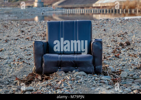 An abandoned living room chair that was discarded on a rocky sandbar in the center of the Sagami River near Ebina in Kanagawa, Japan. Stock Photo