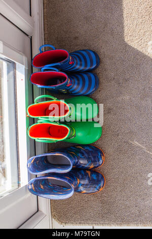 Young childrens colorful wellies sat on a mat by the back door Stock Photo