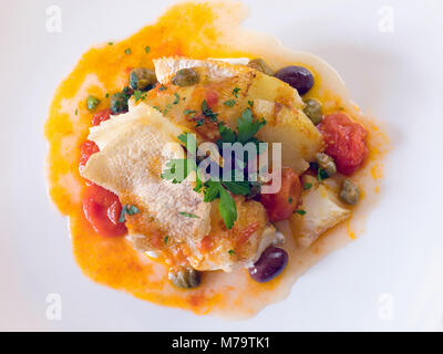 Slice of cod cooked and grilled in a pan with a sauce of cherry tomatoes, olives and capers, a pinch of parsley, oil and salt. Stock Photo