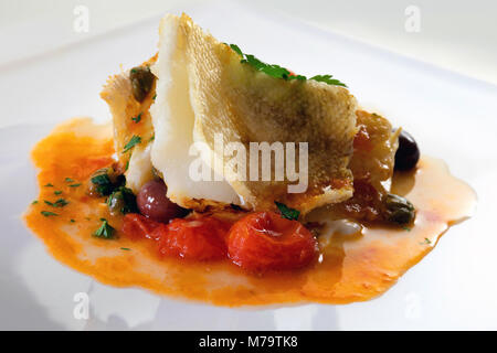 Slice of cod cooked and grilled in a pan with a sauce of cherry tomatoes, olives and capers, a pinch of parsley, oil and salt. Stock Photo