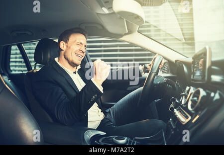 Young businessman in a blazer celebrating success with a fist pump while driving in a car during his morning commute Stock Photo