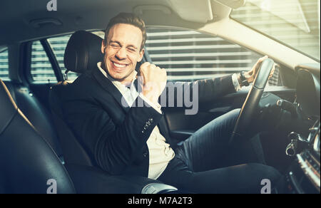 Young businessman in a blazer driving in a car during his morning commute and celebrating success with a fist pump Stock Photo