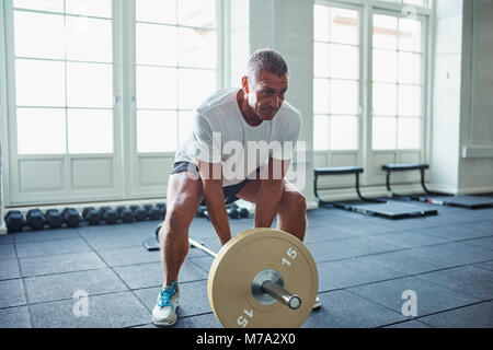 Senior man in sportswear standing alone in a gym focused on lifting weights during a workout Stock Photo