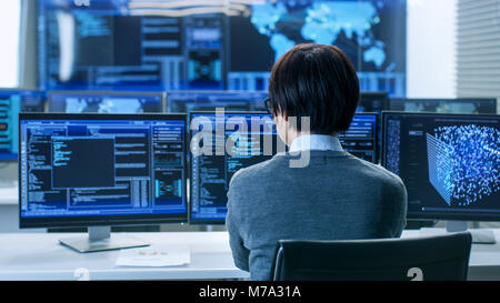 In the System Control Room Technical Operator Works at His Workstation with Multiple Displays Showing Graphics. IT Technician Works on AI research Stock Photo
