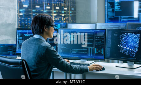 In the System Control Room Technical Operator Works at His Workstation with Multiple Displays Showing Graphics. IT Technician Works on AI research Stock Photo