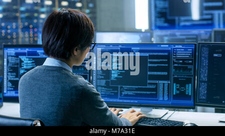 In the System Control Room Technical Operator Works at His Workstation with Multiple Displays Showing Graphics. IT Technician Works on AI research Stock Photo
