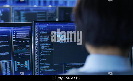 In the System Control Room Technical Operator Stands and Monitors Various Activities Showing on Multiple Displays with Graphics. Administrator Monitor Stock Photo