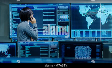In the System Control Room IT Administrator Talks on the Phone. He's in a High-Tech Facility That Works on the Surveillance, Neural Networks, Data Stock Photo