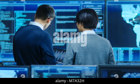 In the System Control Room IT Specialist and Project Engineer Have Discussion, they're surrounded by Multiple Monitors with Graphics. Stock Photo