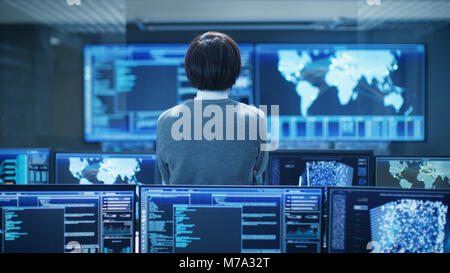 In the System Control Room Technical Operator Stands and Monitors Various Activities Showing on Multiple Displays with Graphics. Stock Photo