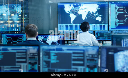 In the System Control Room Operator and Administrator Sitting at Their Workstations with Multiple Displays Showing Graphics and Logistics Information. Stock Photo