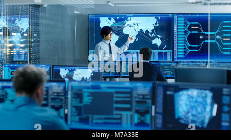 In the System Control Room Manager Holds a Briefing for His Staff Members. They're Work in Data Center and are Surrounded by Multiple Screens Stock Photo