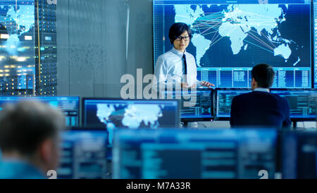 In the System Control Room Manager Holds a Briefing for His Staff Members. They're Work in Data Center and are Surrounded by Multiple Screens Stock Photo