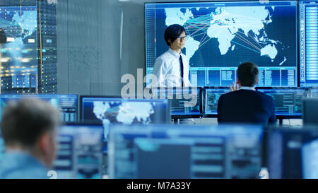 In the System Control Room Manager Holds a Briefing for His Staff Members. They're Work in Data Center and are Surrounded by Multiple Screens Stock Photo