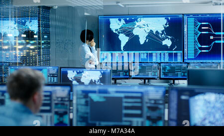 In the System Control Room Chief Engineer Thinks While Standing Before Big Screen with Interactive Map on it. Data Center is Full of Monitors Stock Photo