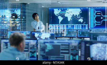 In the System Control Room Chief Engineer Thinks While Standing Before Big Screen with Interactive Map on it. Data Center is Full of Monitors Stock Photo