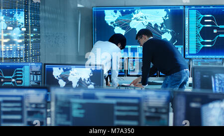 In the System Control Room Project Manage and IT Engineer Have Discussion, they're surrounded by Multiple Monitors with Graphics. Stock Photo