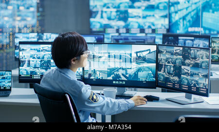 In the Security Control Room Officer Monitors Multiple Screens for Suspicious Activities, He Drinks from a Mug. He's Surrounded by Monitors Stock Photo