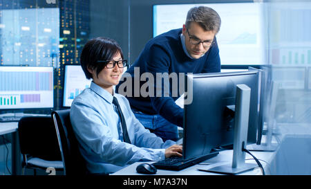 In the Data Mining Center Chief Statistician Consults His Young Assistant sits at His Workstation Surrounded with Monitors Displaying Data and Graphs. Stock Photo