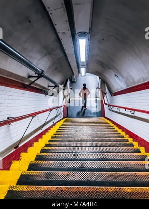 Man rushing down the stairs of the Tube underpass. White ceramic wall tiles and metal staircase with red handrail at Chalk Farm Underground Station. Stock Photo