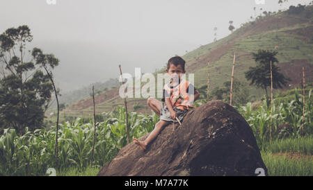A Boy Who Sitting On Rock While Waiting His Parent Farming Stock Photo