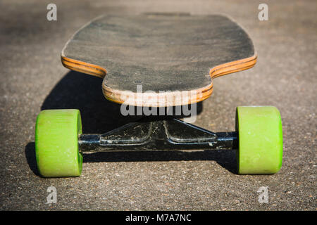 Old used longboard on the ground. Black skateboard on asphalt road. Close up. Stock Photo