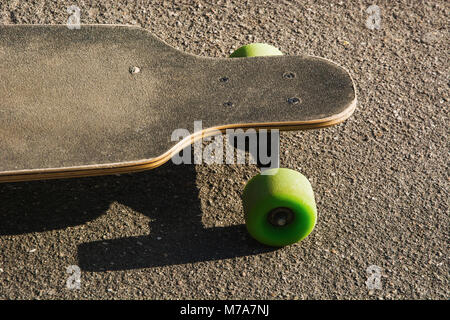 Old used longboard on the ground. Black skateboard on an empty asphalt road. Close up. Stock Photo