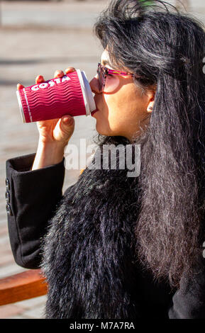 French-Algerian female student Faiza Faa from Paris sitting on the summer seats drinking a cup of Costa Coffee in Dundee city centre, UK Stock Photo