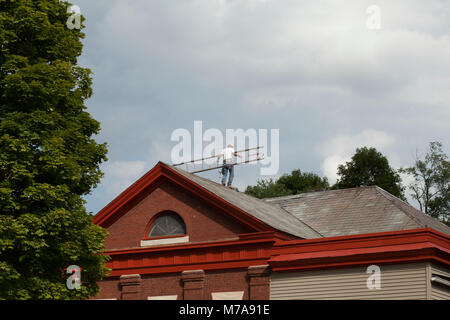 Roofer climbs along the ridge of a slate roofed building. Stock Photo
