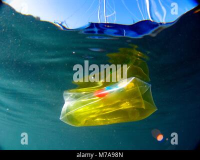 Yellow transparent children toy floating and causing water pollution. Aluminium foil floating and causing water pollution. Water pollution is largely  Stock Photo
