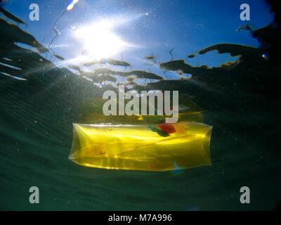 Yellow transparent children toy floating and causing water pollution. Aluminium foil floating and causing water pollution. Water pollution is largely  Stock Photo