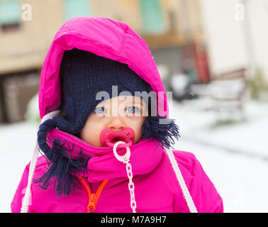 Adorable toddler baby girl in a magenta snow suit playing on the snow. Stock Photo