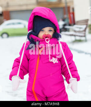 Adorable toddler baby girl in a magenta snow suit playing on the snow. Stock Photo