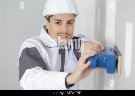 young builder in hardhat sanding wall indoors Stock Photo