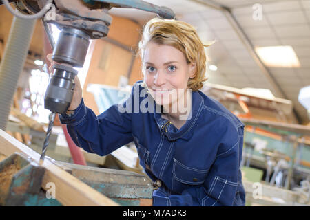 beautiful female carpenter at work using vertical drilling machine Stock Photo
