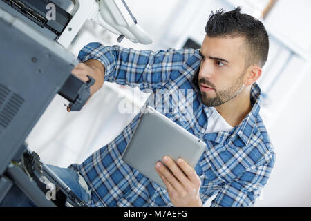 technician using a tablet to fix a printer Stock Photo