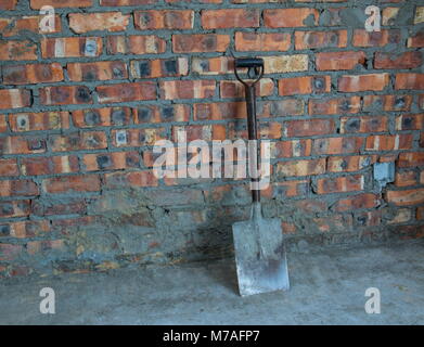 A metal spade rests against a raw brick wall on a building site image in landscape format with copy space Stock Photo