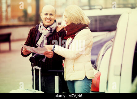 Senior couple of travellers with trollers looking in map on the street Stock Photo