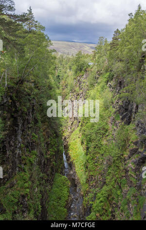 Braemore, Scotland - June 8, 2012: Corrieshalloch Gorge is a deep cut in landscape with forested vertical slopes under gray cloudscape. Stock Photo