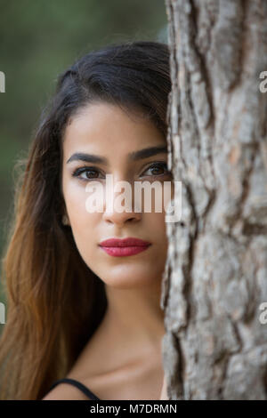 Serious young woman hiding behind a tree Stock Photo