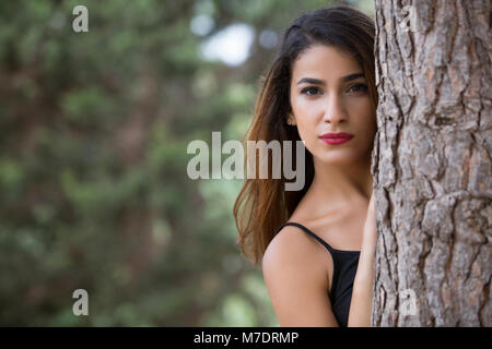 Beautiful young woman hiding behind a tree Stock Photo