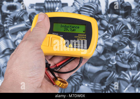 Detail of hand with digital meter of electric passive components. Idea of professional work in the electronics industry. Gray-blue coils on background. Stock Photo