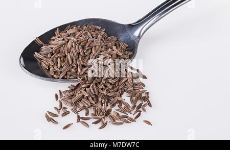 Close-up a spoonful of aromatic caraways. Carum carvi. Pile of brown cumin seeds on the stainless steel spoon partially spilled on a white background. Stock Photo