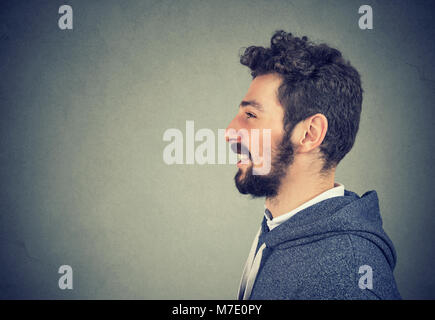 Side view of young hipster man with beard laughing and looking away on gray background. Stock Photo