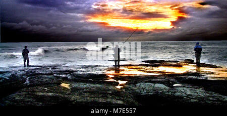 Three men fish off the rocks at sunset in Newprt RI USA photo bill belknap Stock Photo