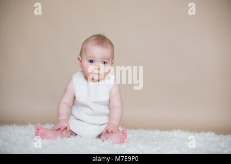 Close portrait of cute little baby boy, isolated on beige background, baby making different facial expressions, crying, sad, smiling, laughing Stock Photo